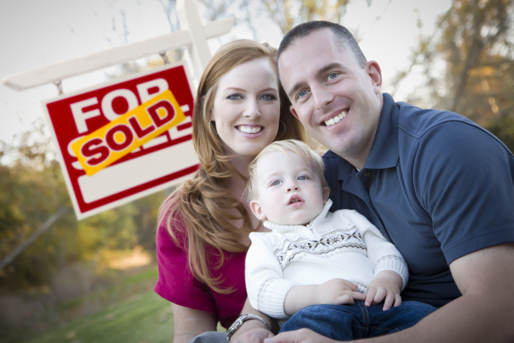 Happy Young Caucasian Family in Front of Sold Real Estate Sign