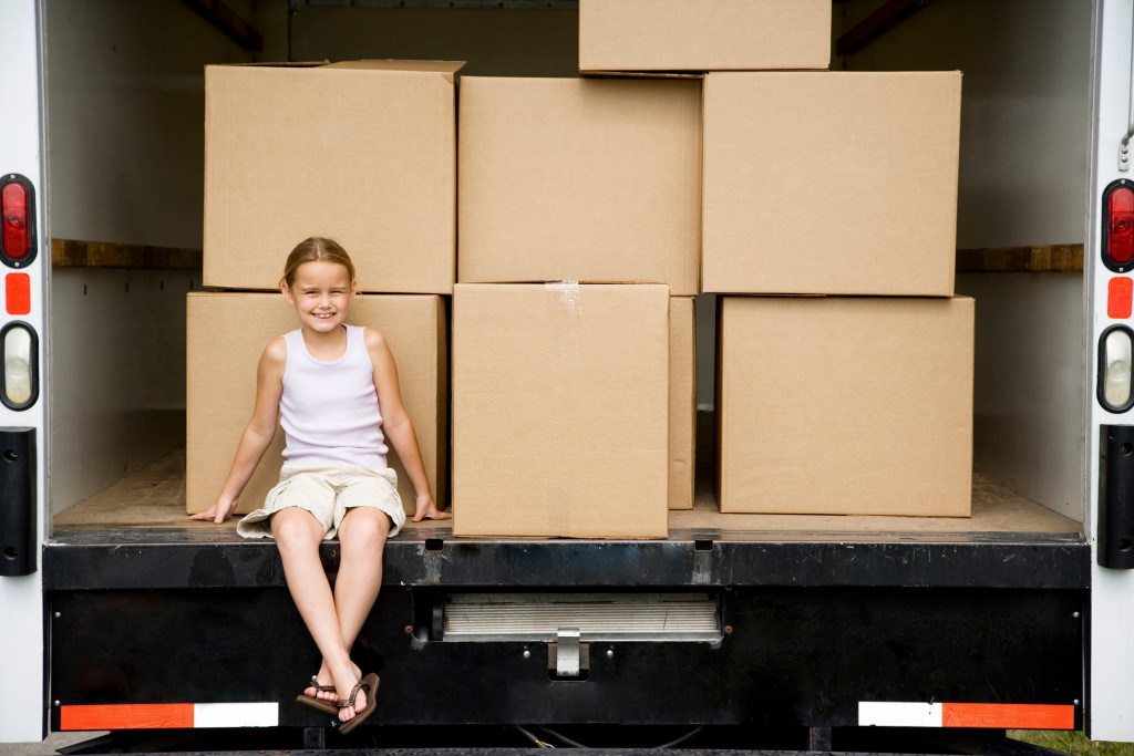 young girl smiling while sitting at the back of a moving company truckl